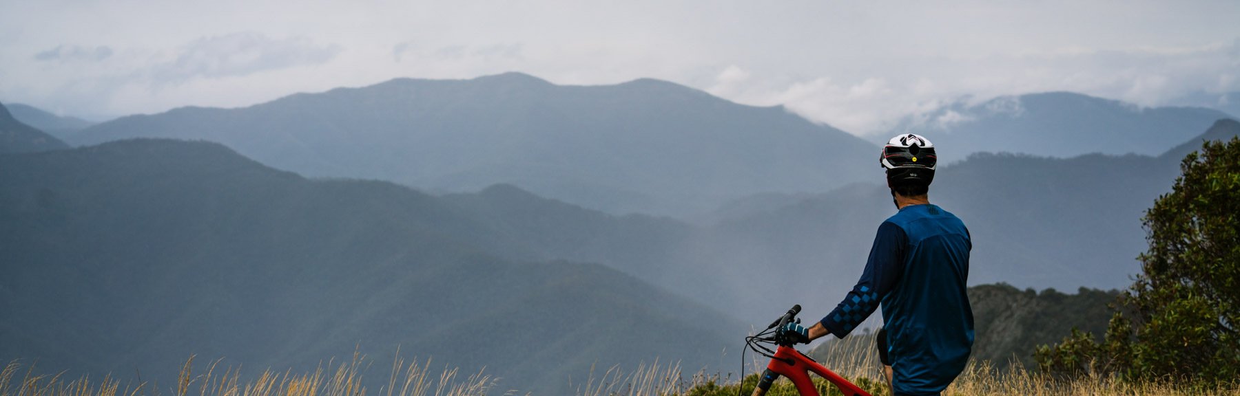 Mountain bike rider pauses on the trail to take in the view across the high country. Image FLOW Mountain Bike