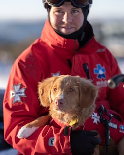 Therapy dog in training, Chilli, with handler Campbell. Both in red ski patrol jackets