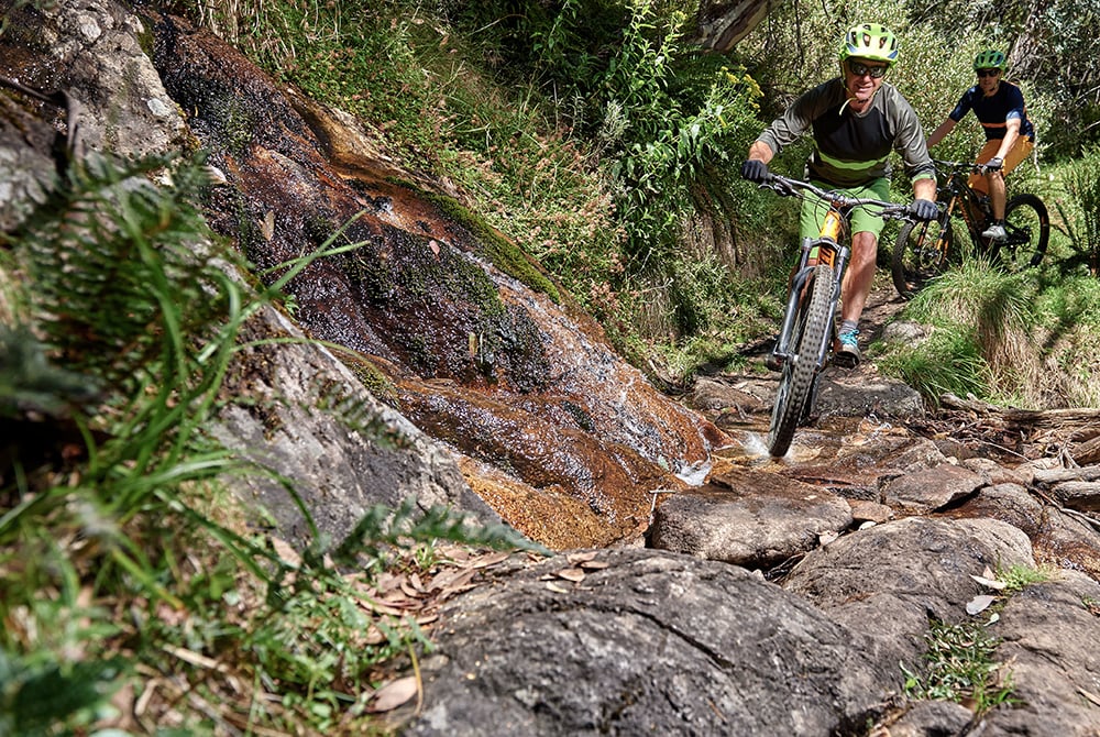 Two mountainbikers ride over large granite boulders on one of Mt Buller's iconic bike trails