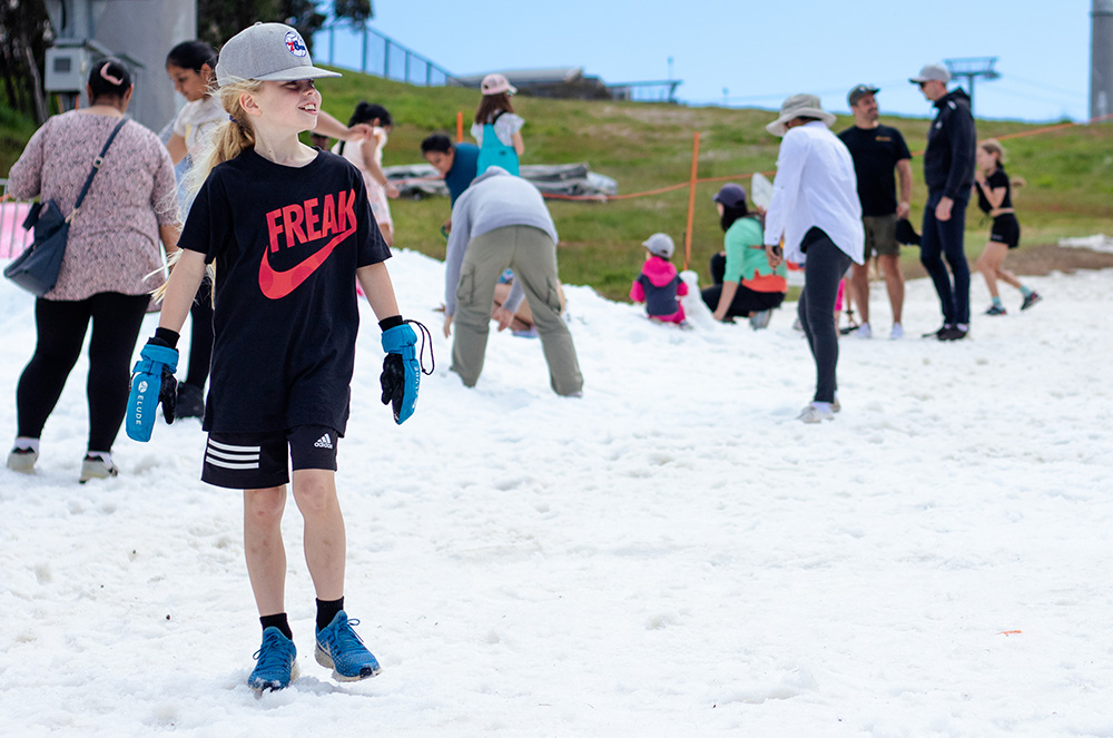A child wearing shorts, t-shirt and sunhat is playing on snow on a summer day at Mt Buller