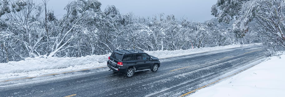 Car driving along the Mt Buller road during a snowy winter day past snow drifts and snow covered gumtrees